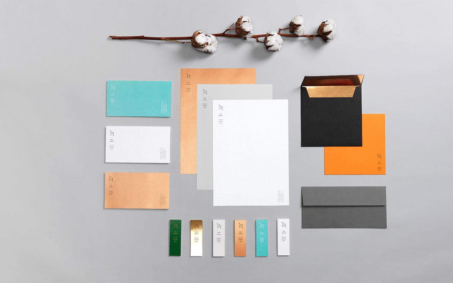 Stationery in cream, copper, turquoise and charcoal laid out beside a cotton branch